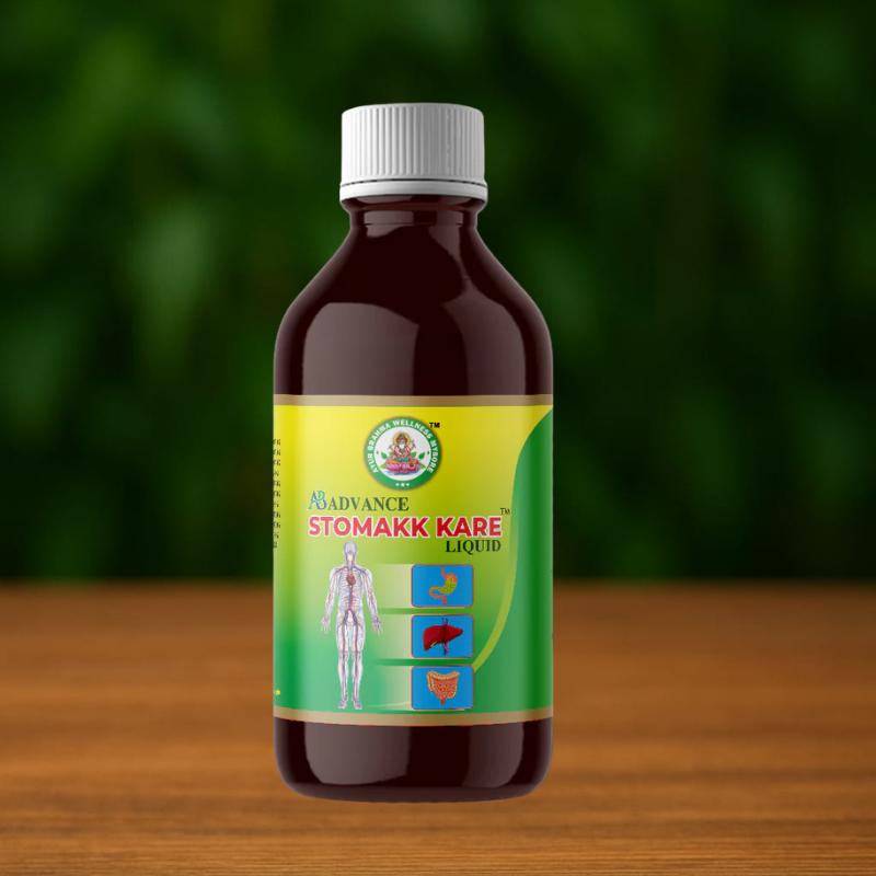 A brown bottle with a white cap labeled Ayur Brahma Stomach Kare Liquid, adorned with stomach, liver, and intestine icons, sits on a wooden surface against a blurred green background.